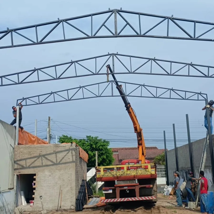 Guindaste erguendo tesouras de estrutura metálica numa obra da Serralheria União